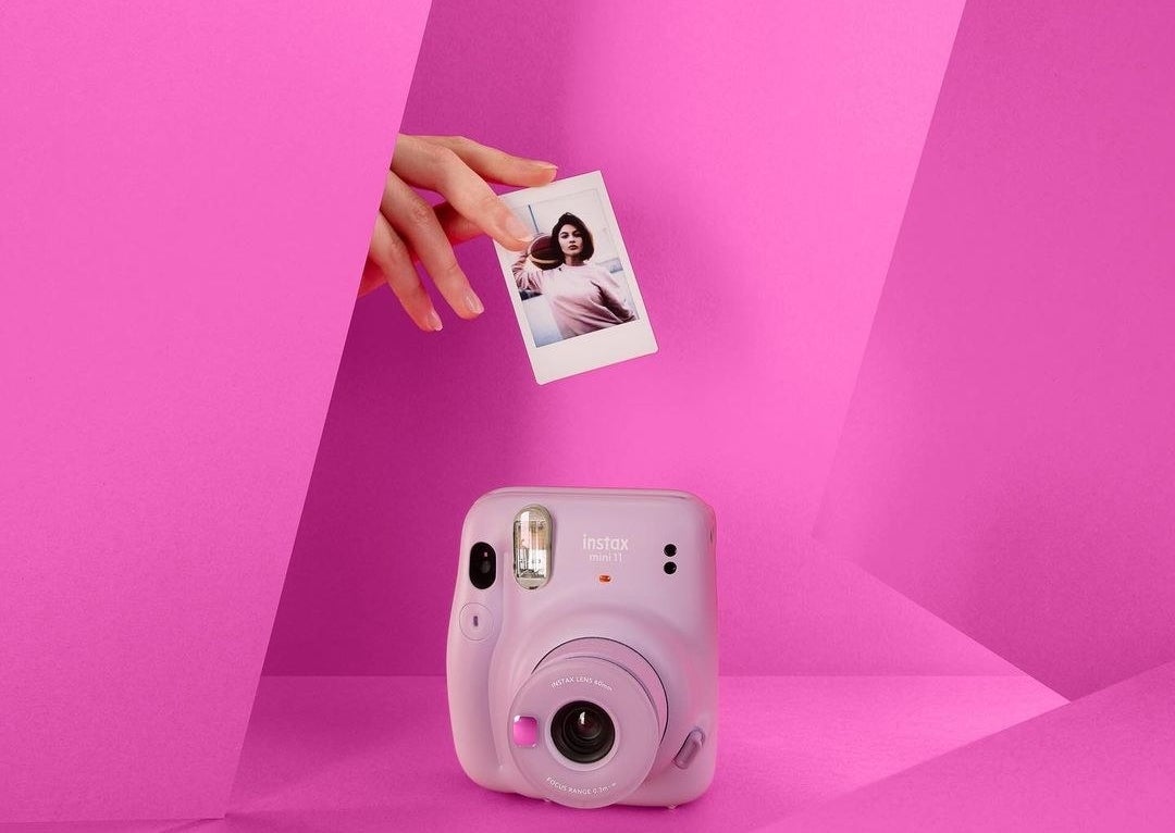 An instant camera with a person&#x27;s hand holding a photograph above it