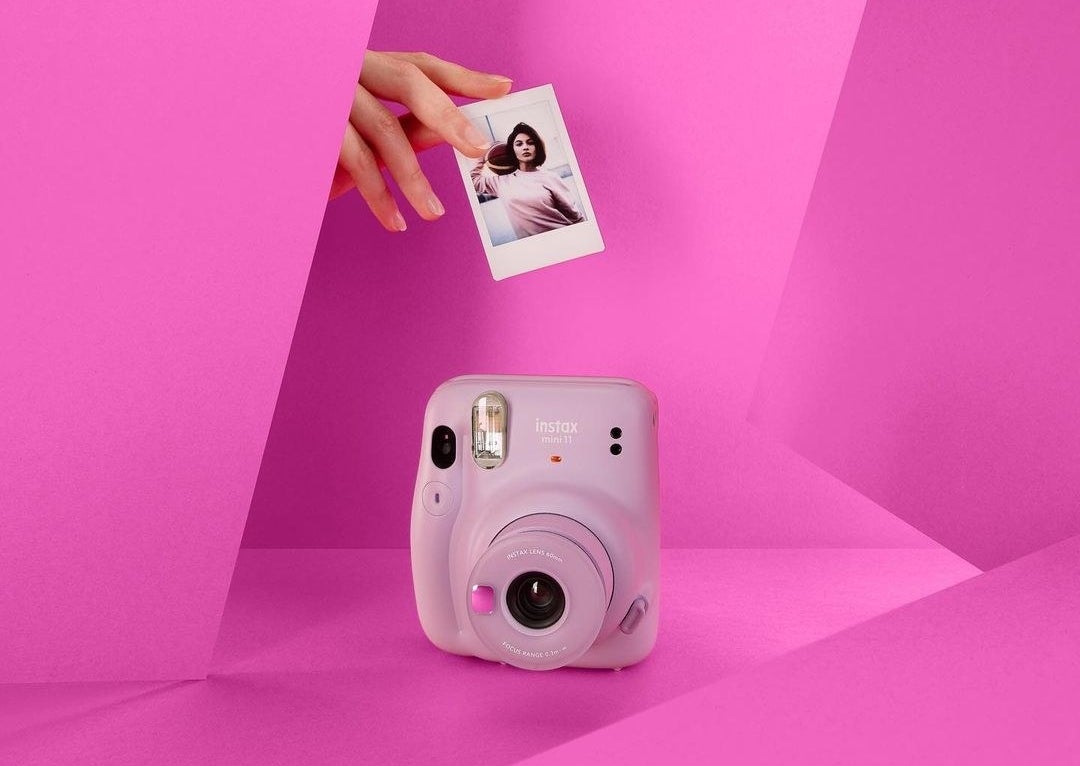 An instant camera with a person&#x27;s hand holding a photograph above it