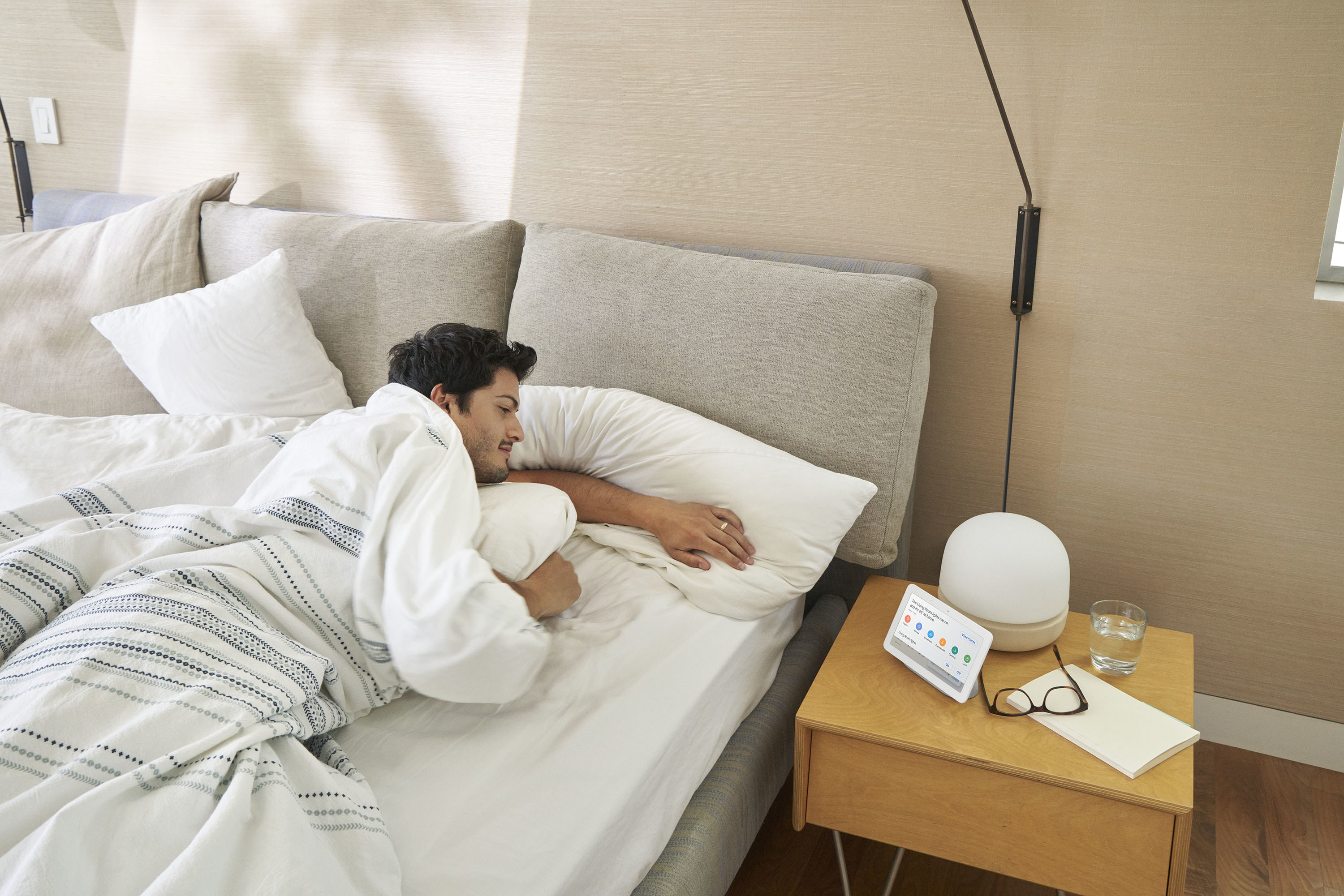 Man lying in bed looking at Nest Hub on nightstand. 