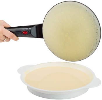 A hand holding the crepe maker by the handle after taking it out of the bowl of batter