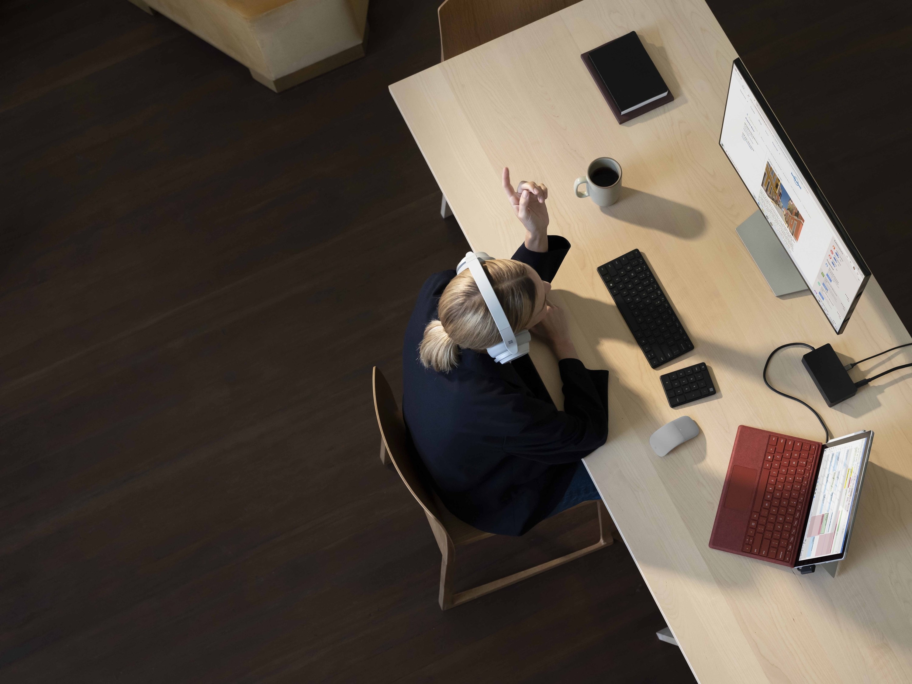 A person wearing headphones and working on a large monitor and the Surface pro 7