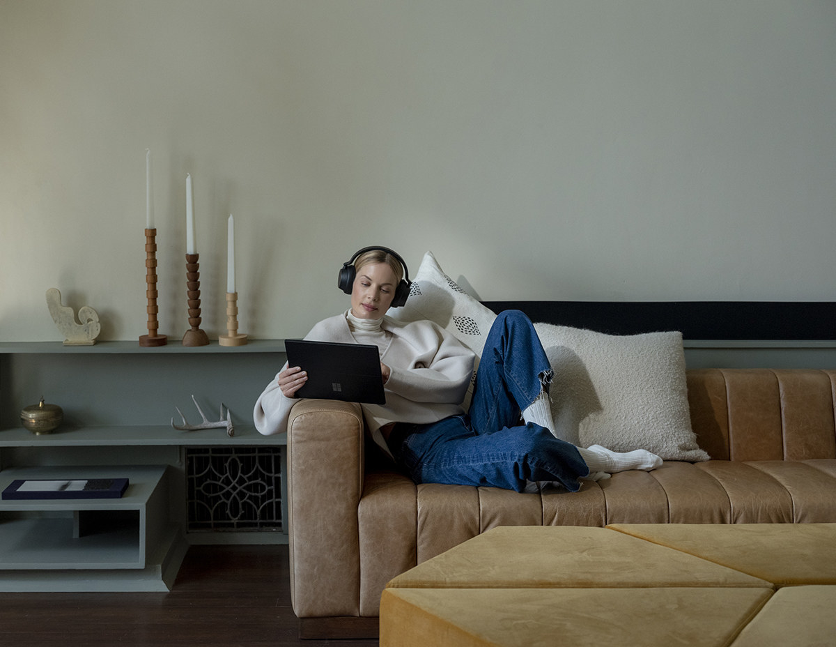A person wearing headphones and using the laptop while lounging on a sofa