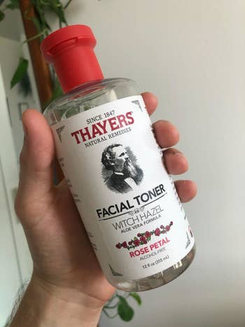A reviewer holding the red and white bottle which says the toner has been in production since 1847