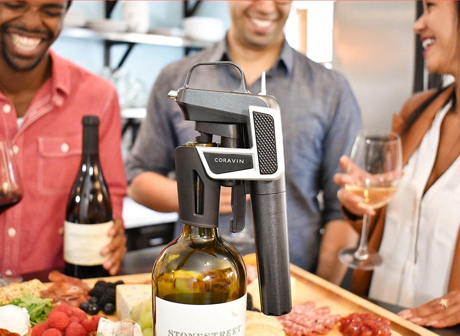 The wine opener on a bottle of wine with people gathered around it drinking glasses of wine