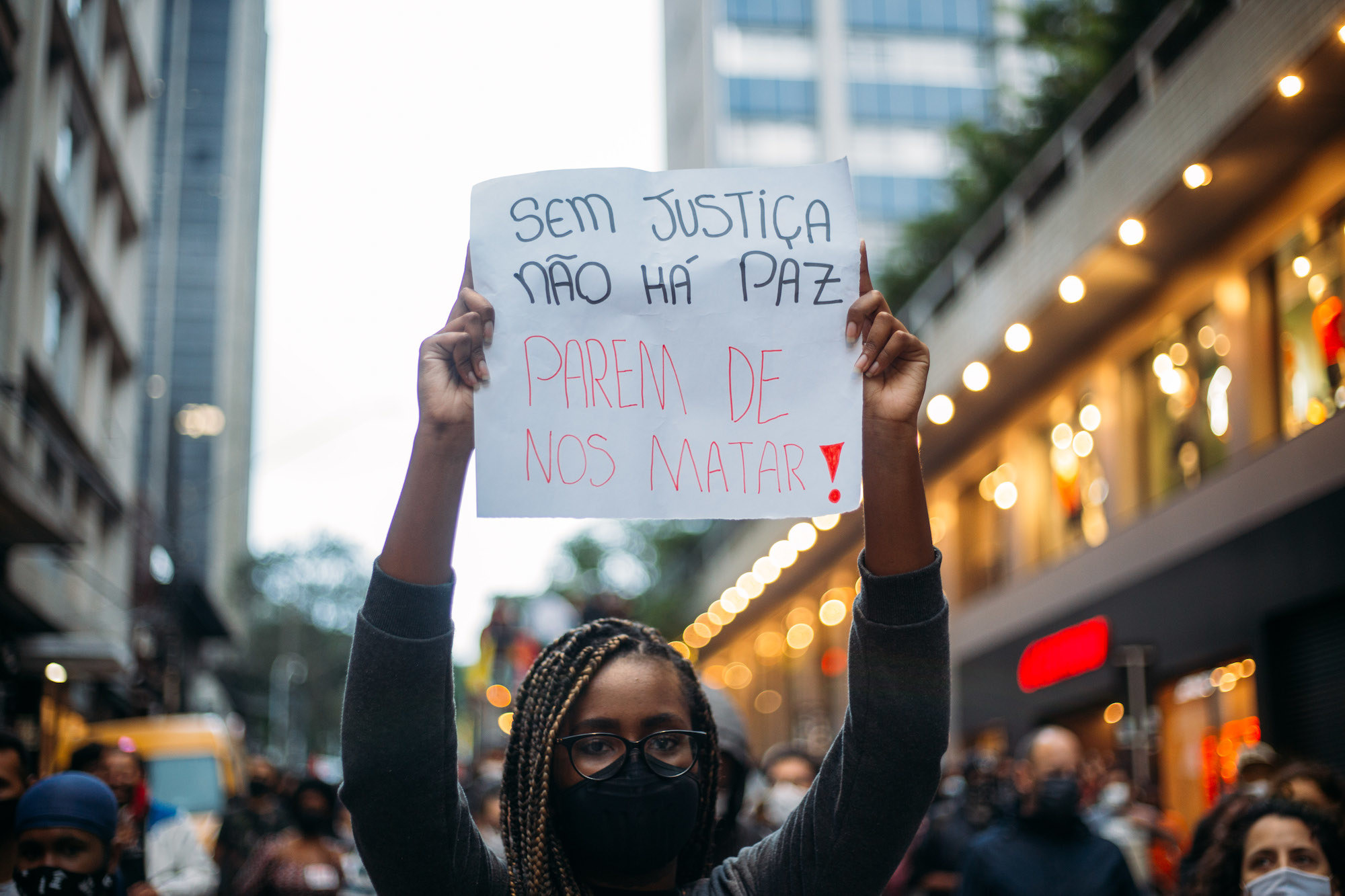 Mulher negra usando tranças e segurando cartaz onde se lê "sem justiça não há paz, parem de nos matar""