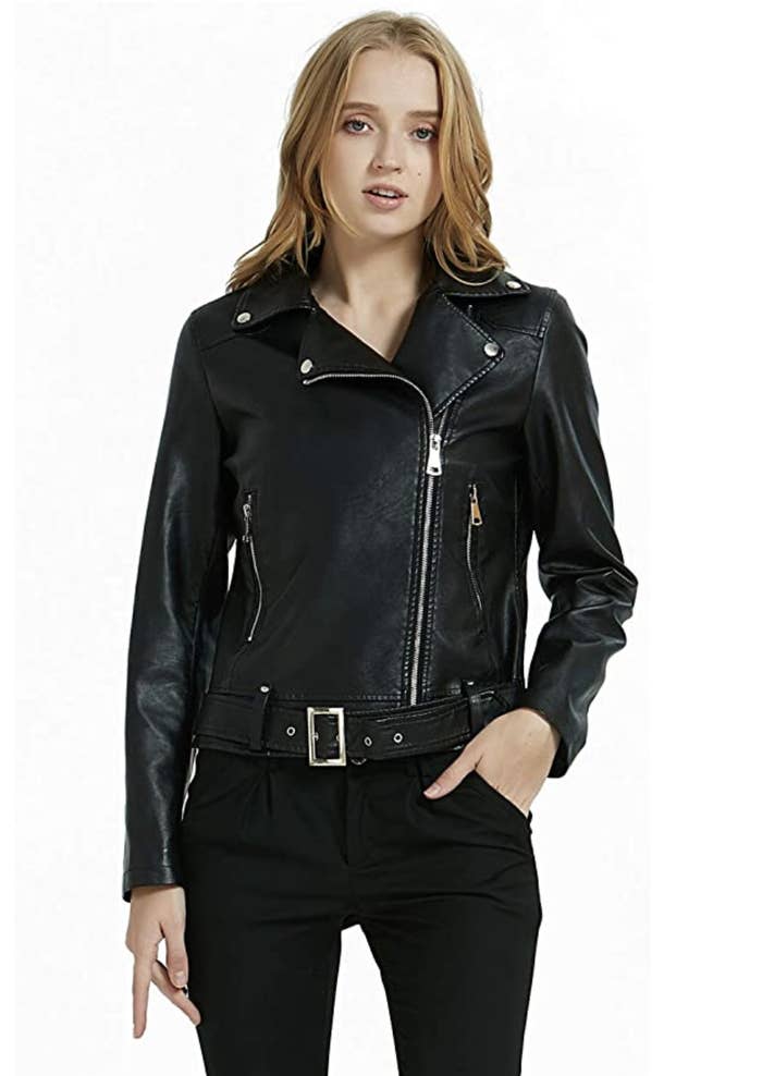 A model in a black zip up faux leather jacket with an asymmetrical front zip closure and belt at the bottom 