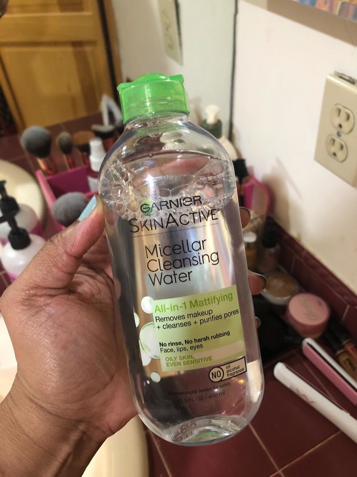 A reviewer holding the bottle which says it&#x27;s suitable for oil and sensitive skin