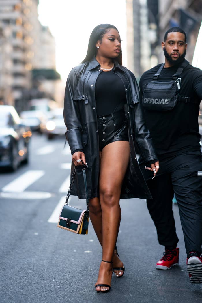 Megan Thee Stallion in shorts and a black trench coat, with a man on her right also in black, in New York