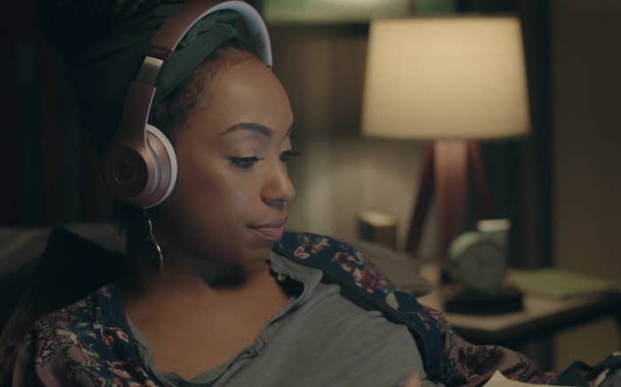 A girl sits on her bed wearing headphones, looking at a laptop.