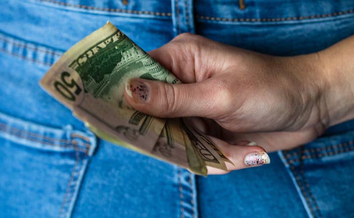 Image of woman&#x27;s hand holding money in front of jeans