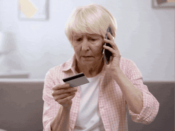 GIF of old woman shrugging confusedly at credit card while on phone 
