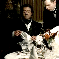 Gif of Sherlock Holmes putting a napkin in his collar before eating a fancy meal 
