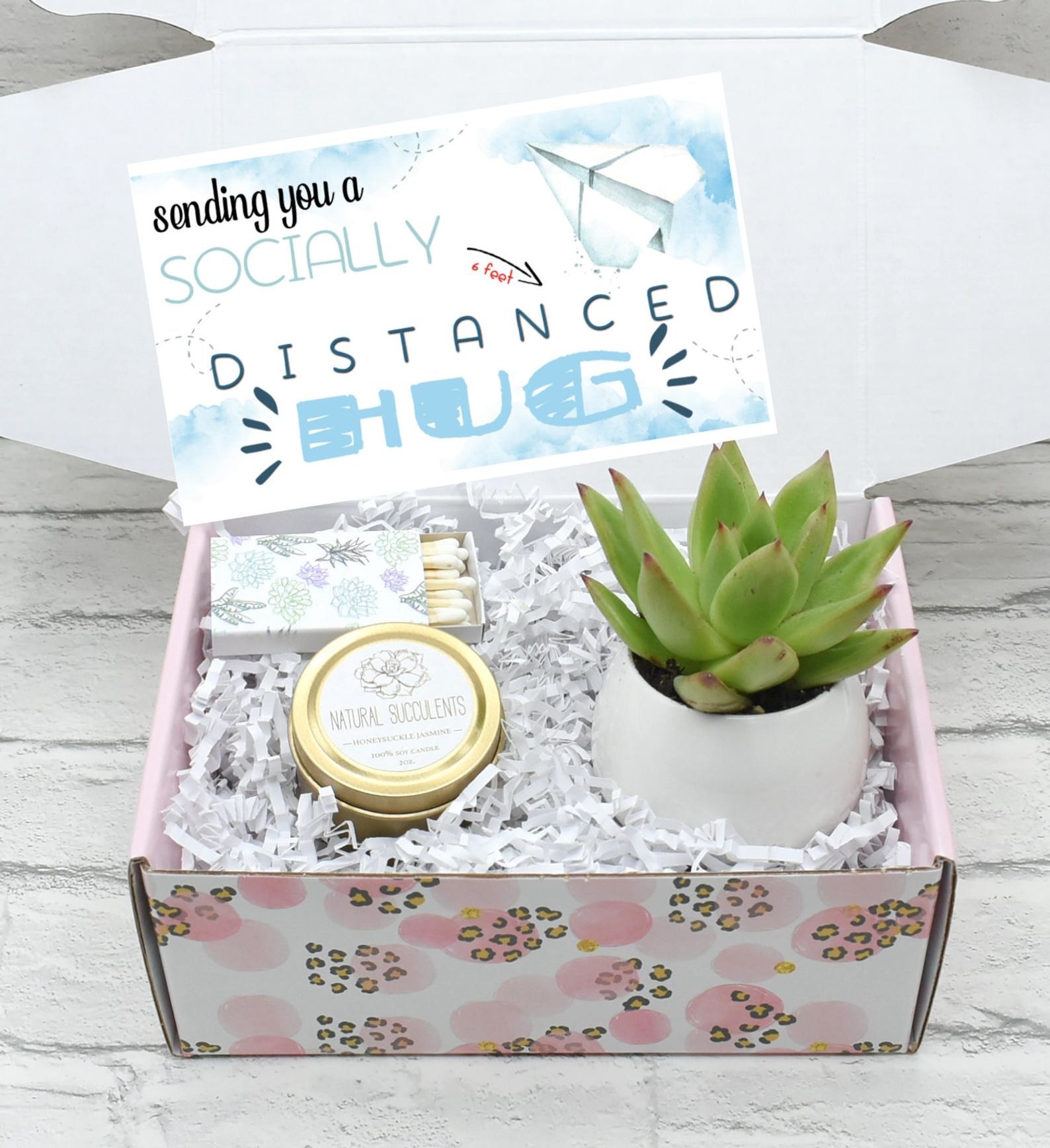 A care package filled with a planted succulent, candle, and matches with a note that reads &quot;sending you a socially distanced hug&quot;