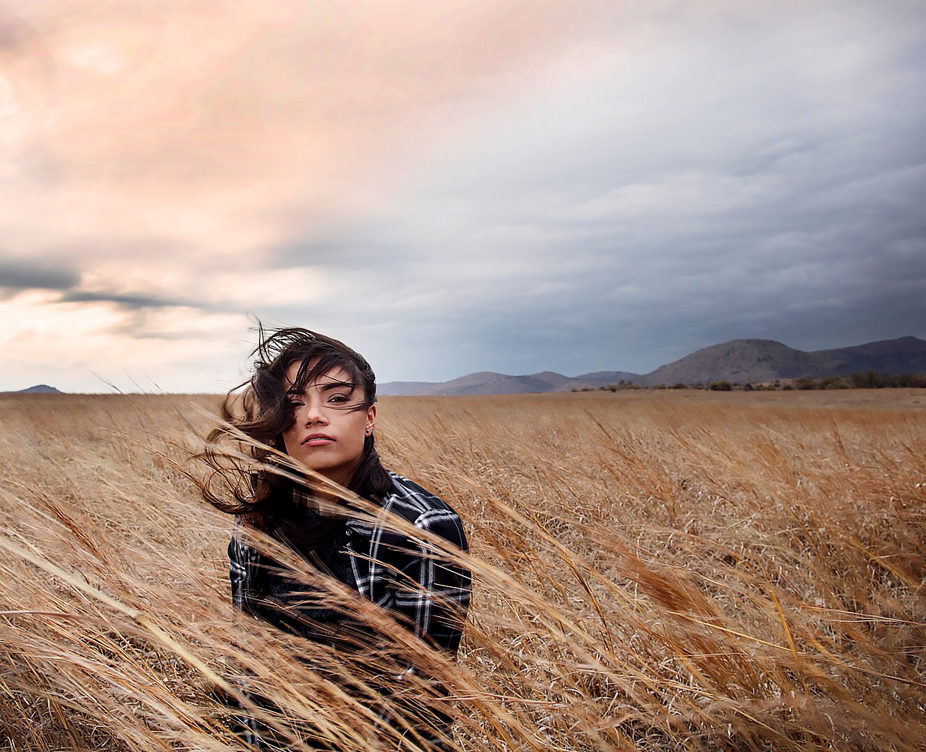 A women with windswept hair in a field under a cloudy sky