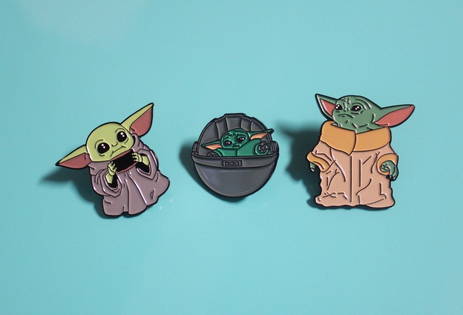 three Yoda pins. The first is Baby Yoda holding a cup. The second is Baby Yoda sitting inside of the Death Star. The third is adult Yoda.