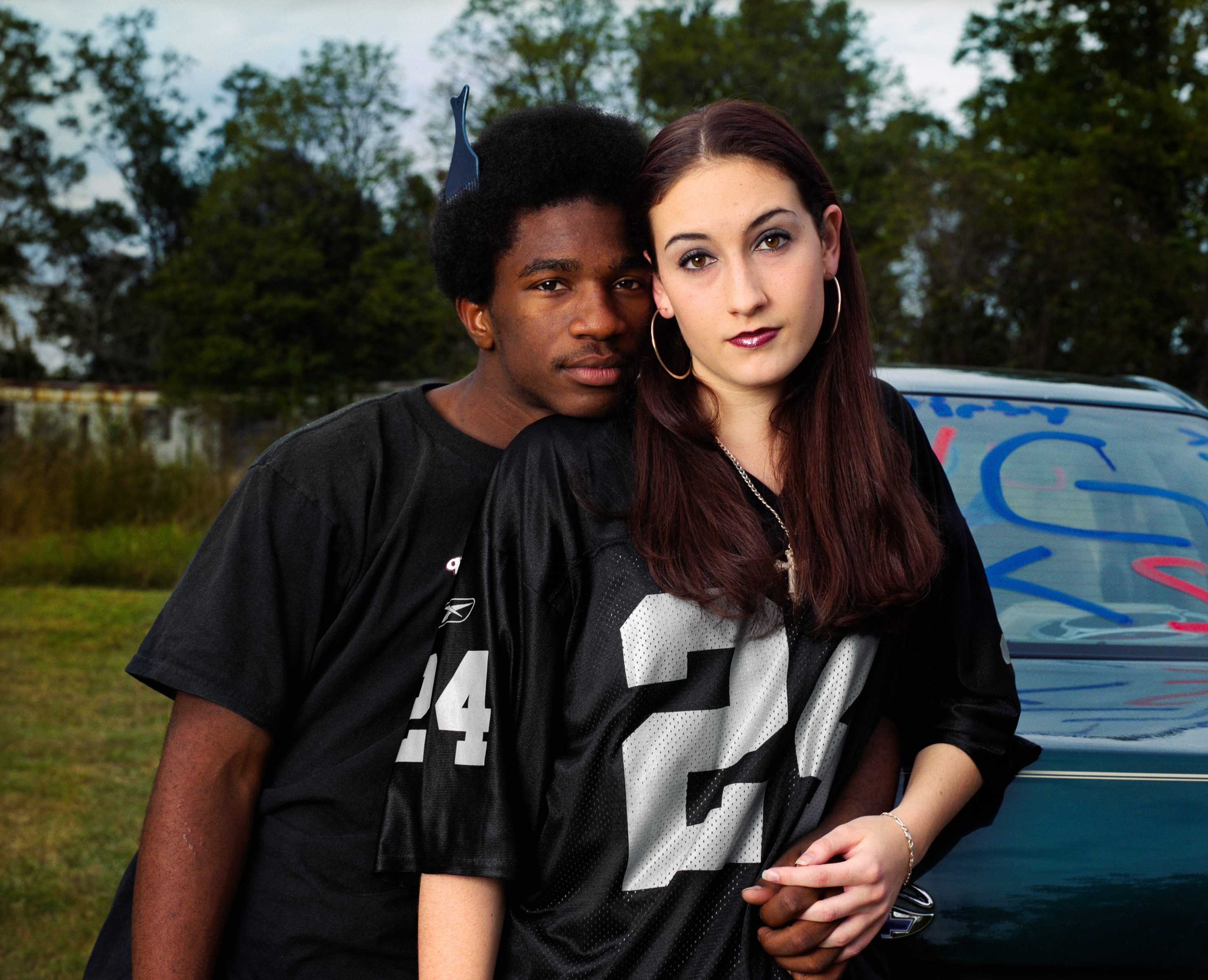 A black teenager with an afro and his arm around a white girl in a football jersey