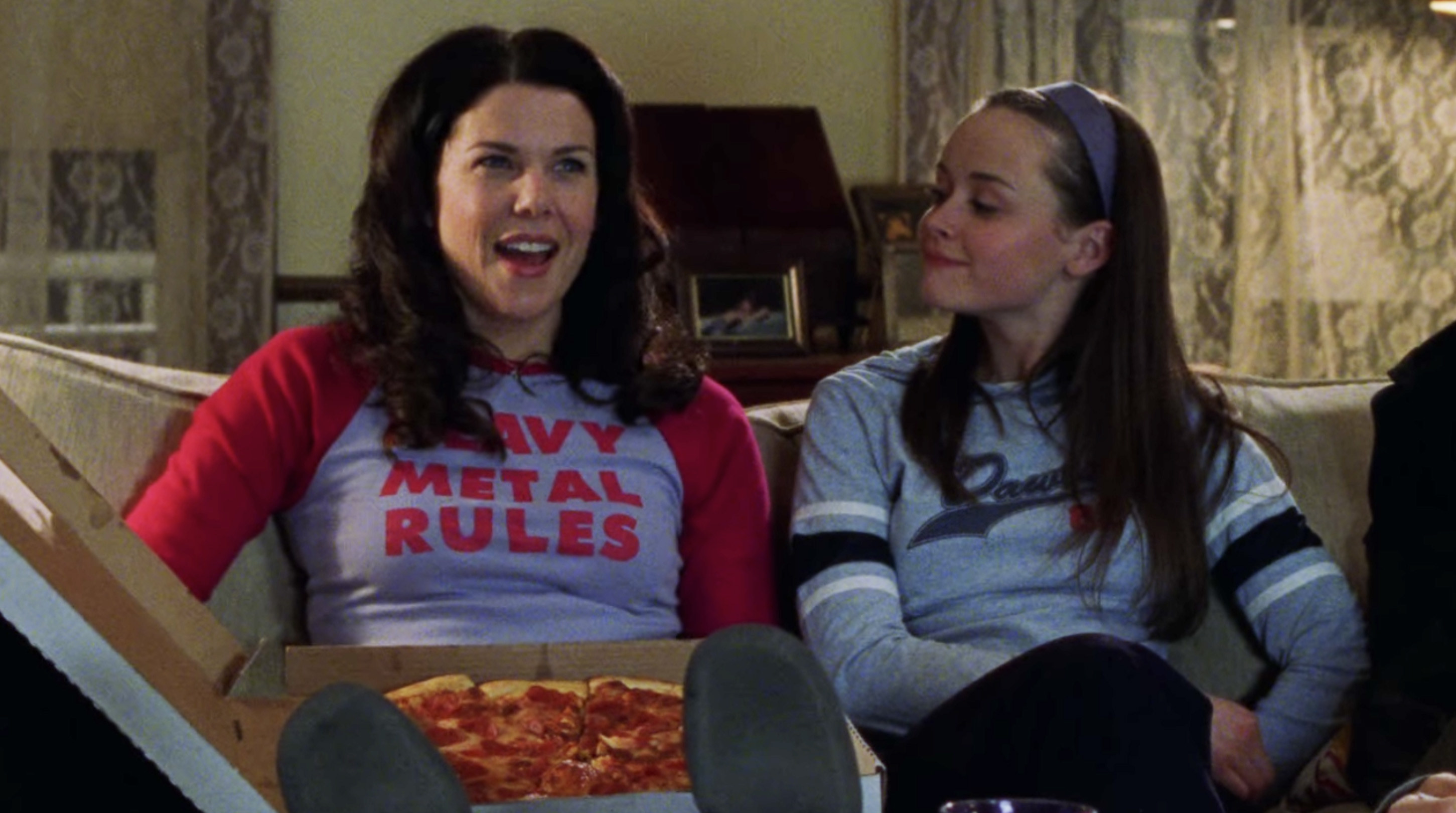 Lorelai and Rory sitting on the coach eating pizza