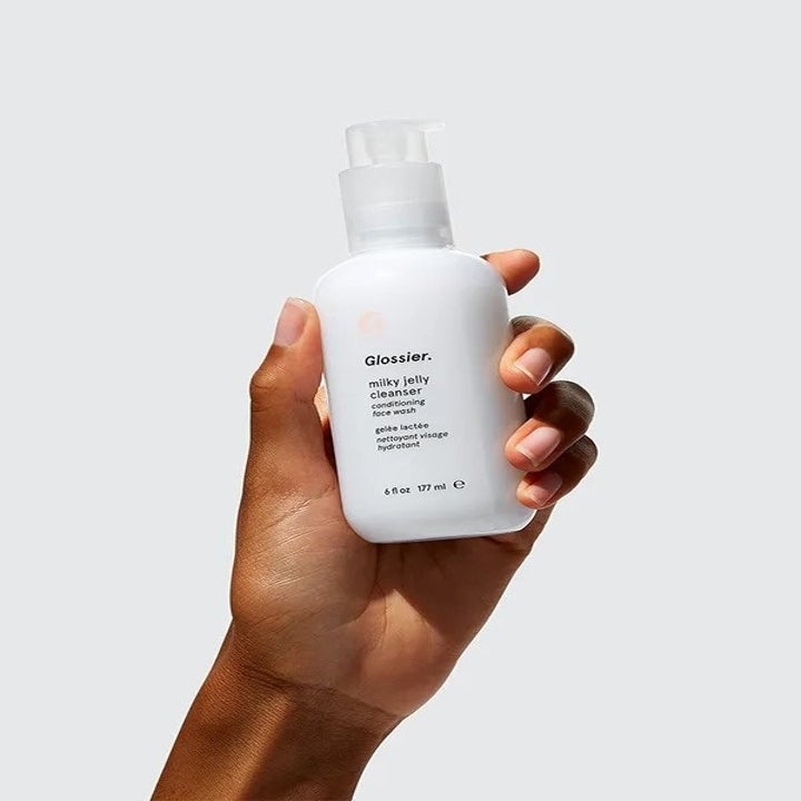 Hand holds white bottle that says "Glossier Milky Jelly Cleanser"