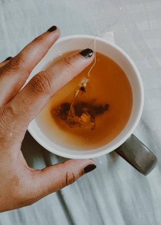 A hand over a cup of tea with the tea bag inside.
