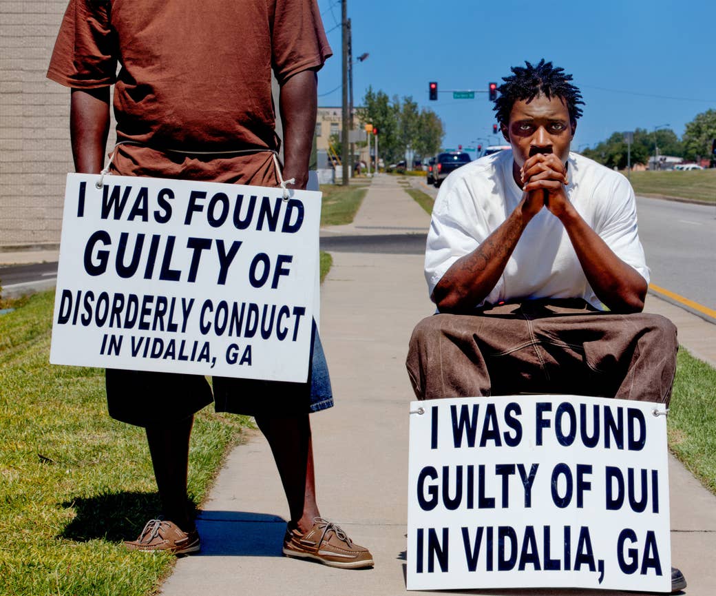 Two black men with signs around their waists on a sidewalk next to a road