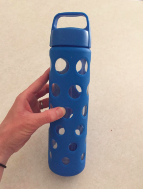 reviewer holding a glass water bottle with blue silicone covering