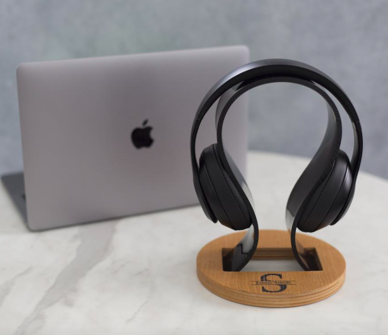 A curved headphone stand on a marble surface next to a laptop