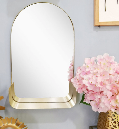 Arched mirror with a gold trip and a small gold shelf on the bottom