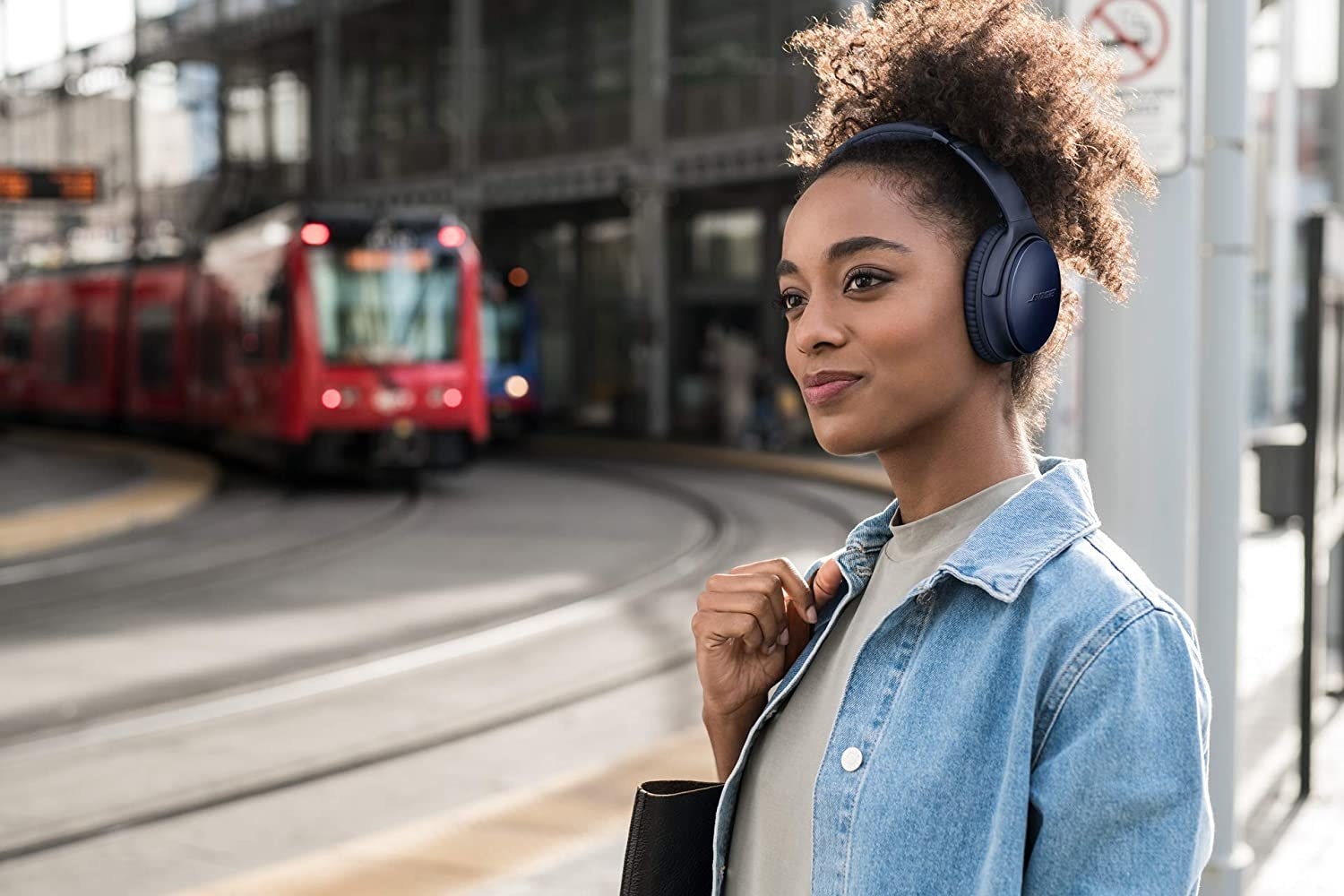 A smiling person waiting for the streetcar while wearing the headphones