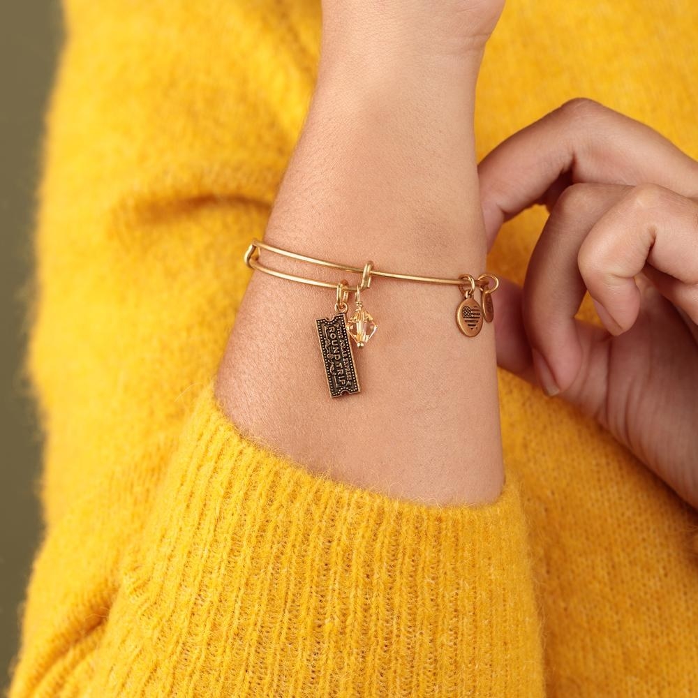 a model wearing a thin gold bangle with a tiny train ticket charm