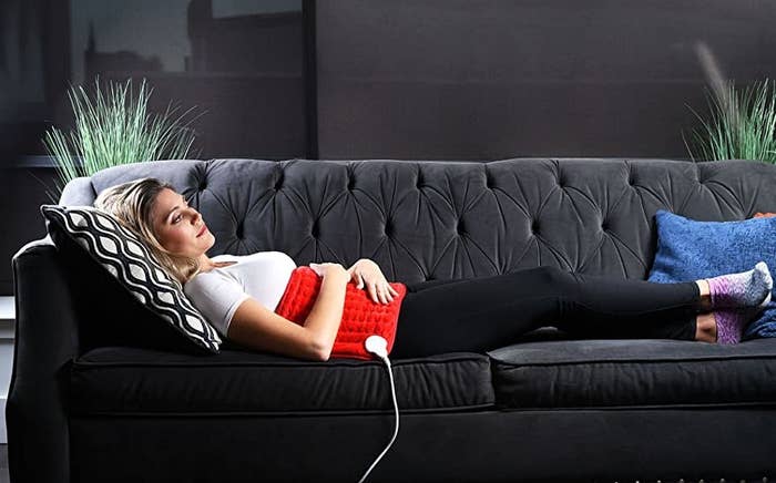 a model lays on a couch with the electric heating pad on their stomach