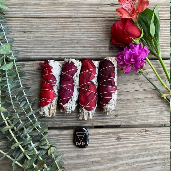 four sage smudges with rose petals wrapped around them sitting beside eucalyptus leaves