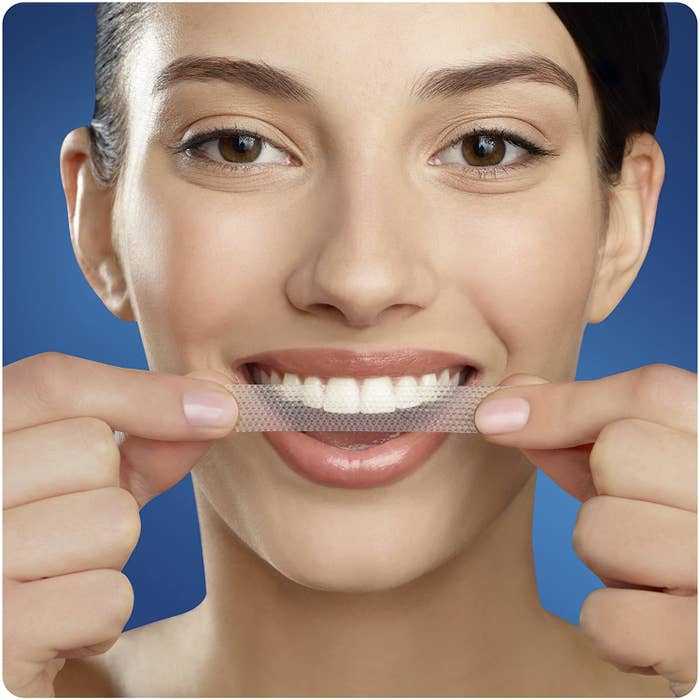 A person placing a whitening strip on their teeth