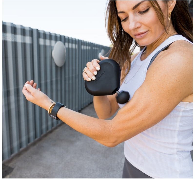 Model using the all black percussive massager on their arm