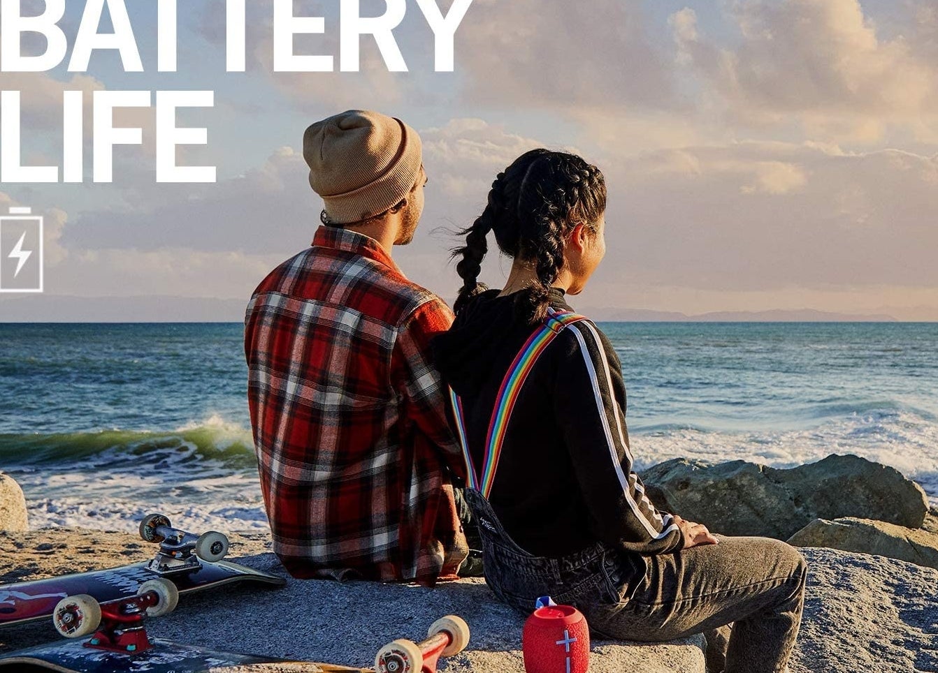 Two people sitting on rocks near a beach with a small speaker behind them