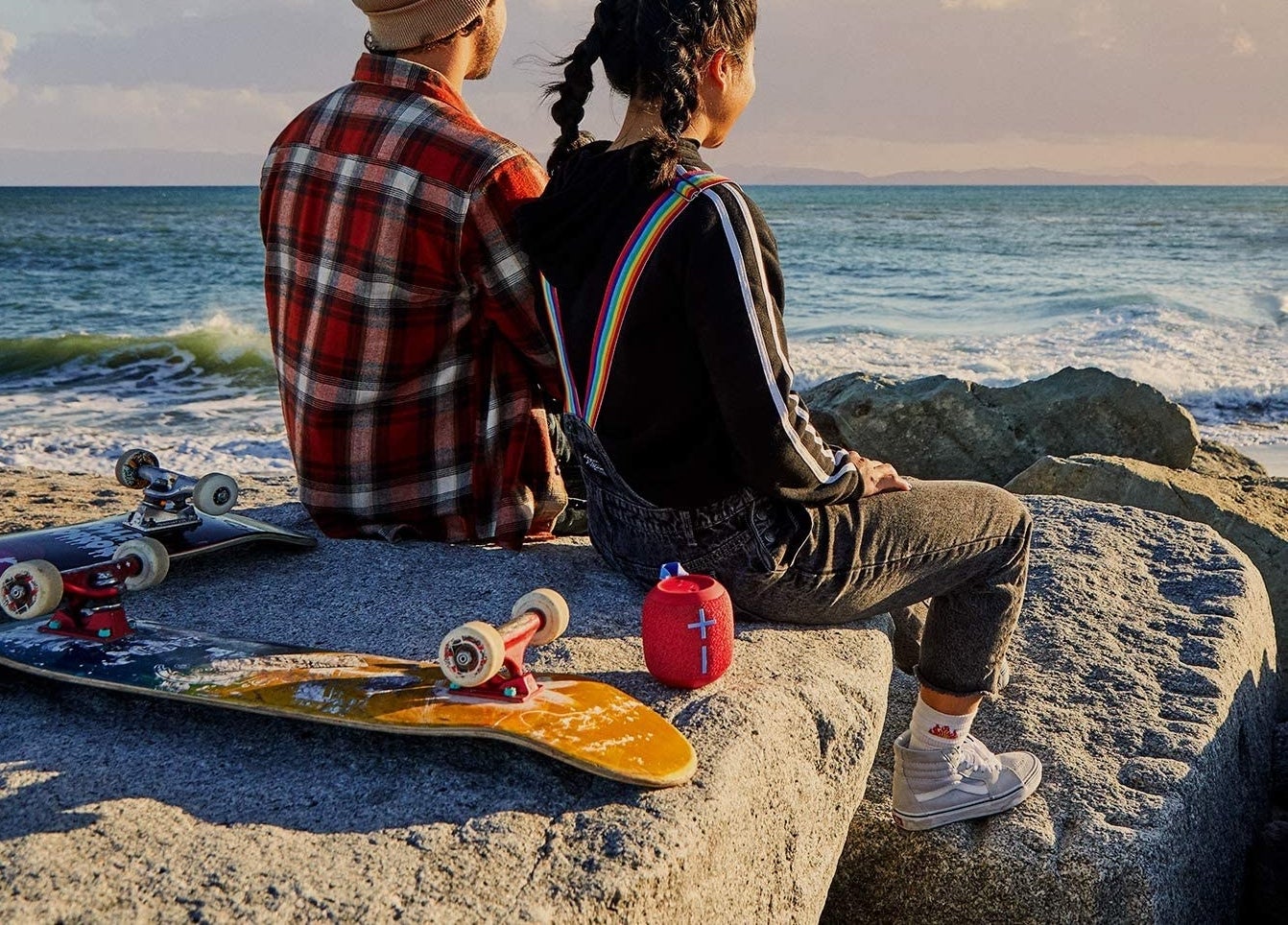 Two people sitting on rocks near a beach with a small speaker behind them