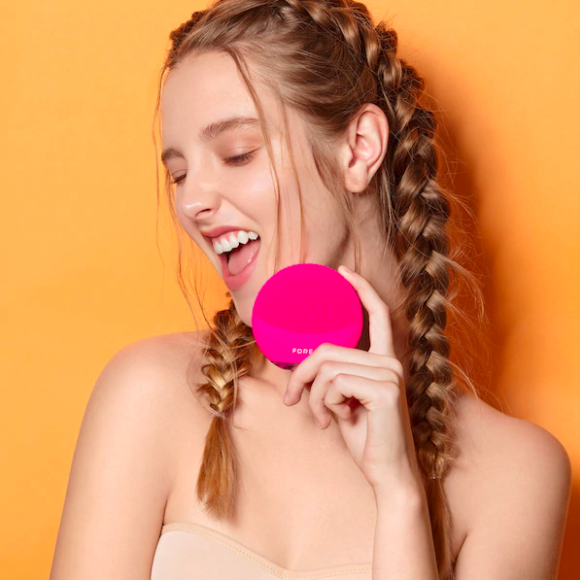 A smiling person holding the facial brush against their face