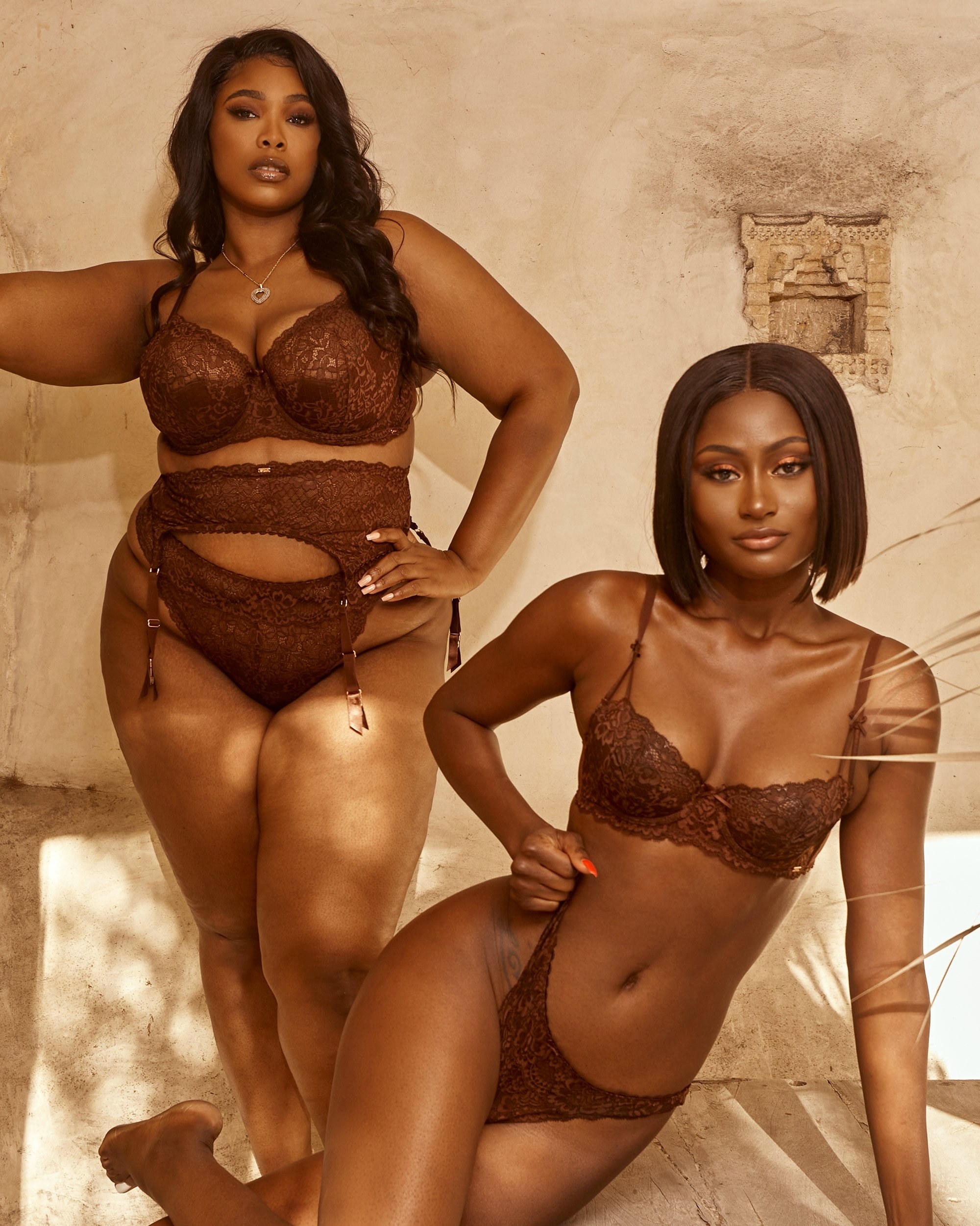 a plus-size and straight-sized model posing in the same lace, chocolate brown lingerie. The plus-size model is also wearing the garter belt that comes with it.