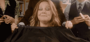 GIF of Melissa McCarthy getting her hair and makeup done and looking happy