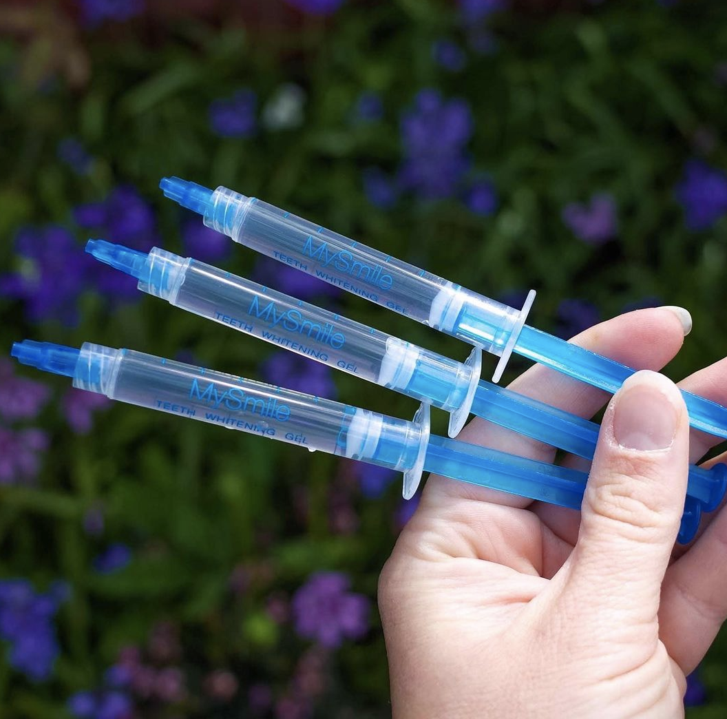 A person holding three gel syringe pens with flowers in the background