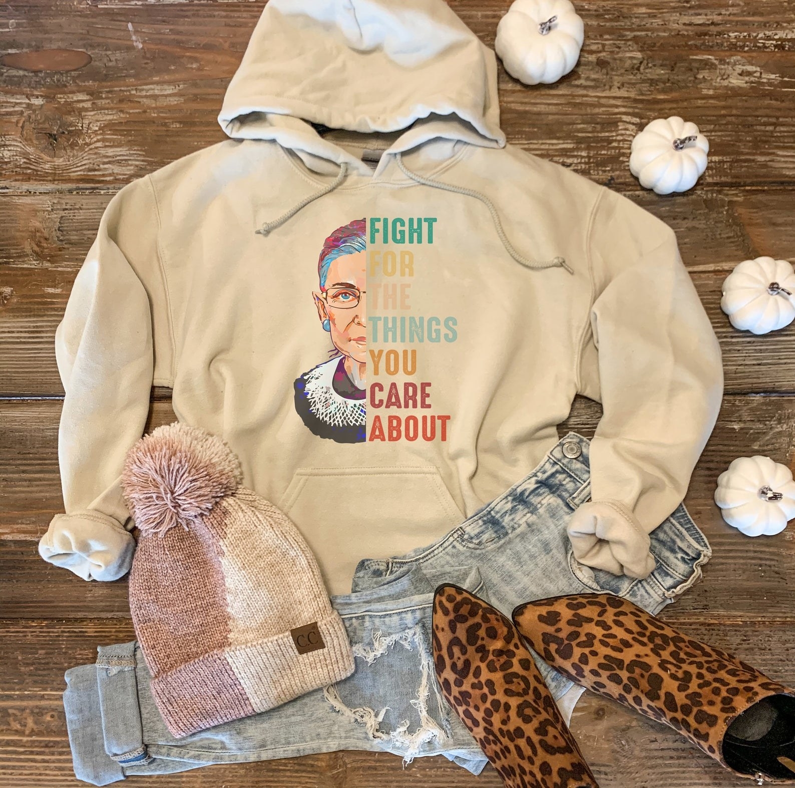 tan hoodie with a graphic design that shows an animated version of half of Justice Ginsburg&#x27;s face and the other half (where her face would be) has a quote that says &quot;Fight for the things you care about.&quot; Sweet!