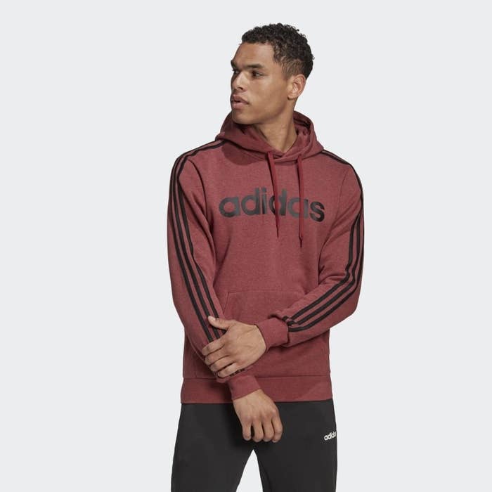 A person wears a hoodie with the Adidas printed on the front and three stripes down each arm