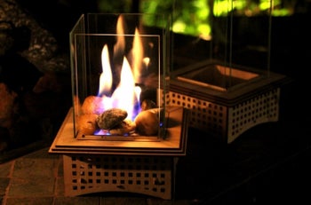 wooden square bottom with rocks on top of it and a flame on top of them with glass around it (four walls of glass)