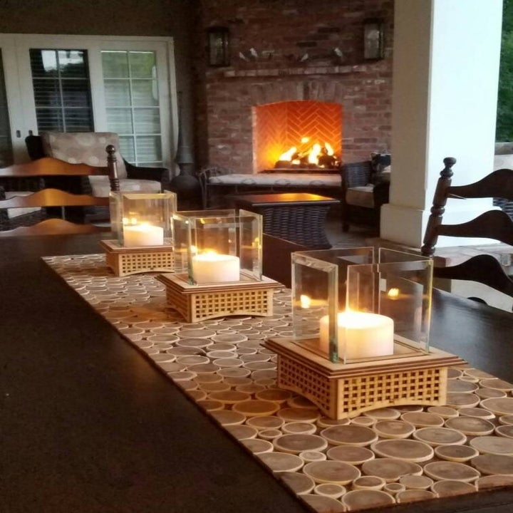 four of the tabletop fireplaces lined on a table runner with candles inside of them lit