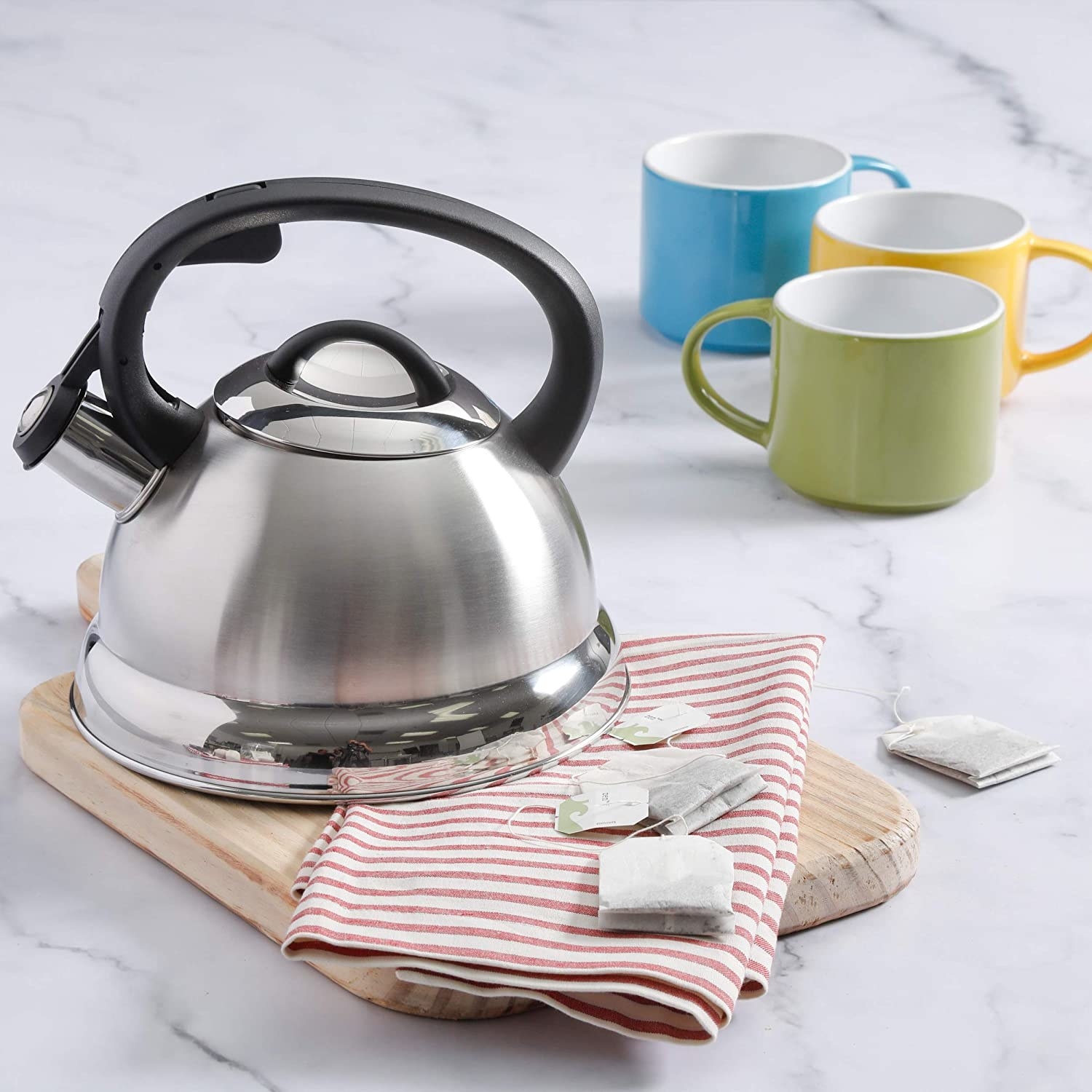 A kettle on a cutting board with tea bags