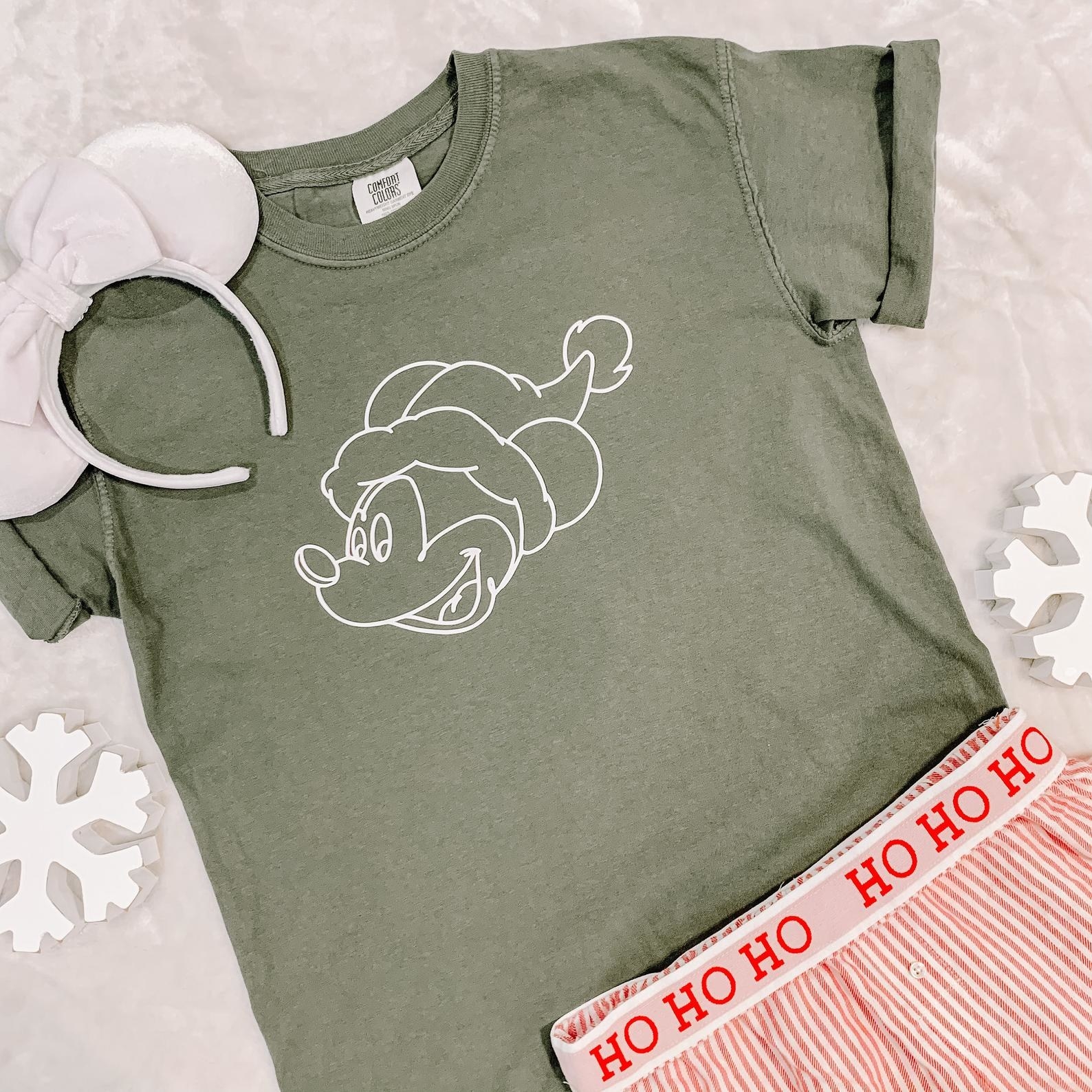 a green tee with a white sketch of mickey wearing a santa hat