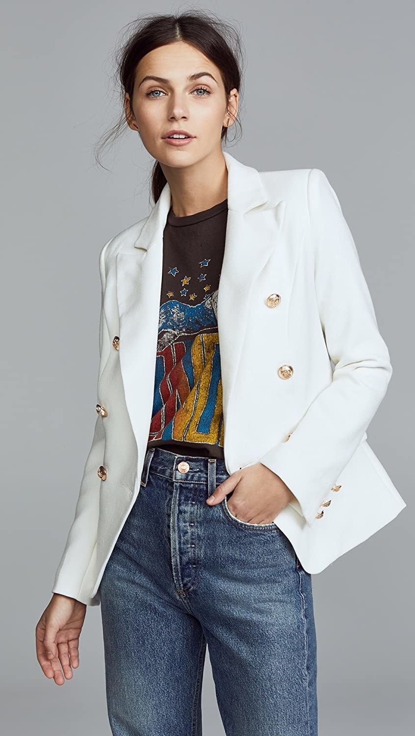 Person wearing white blazer with gold buttons with jeans and a graphic tee 