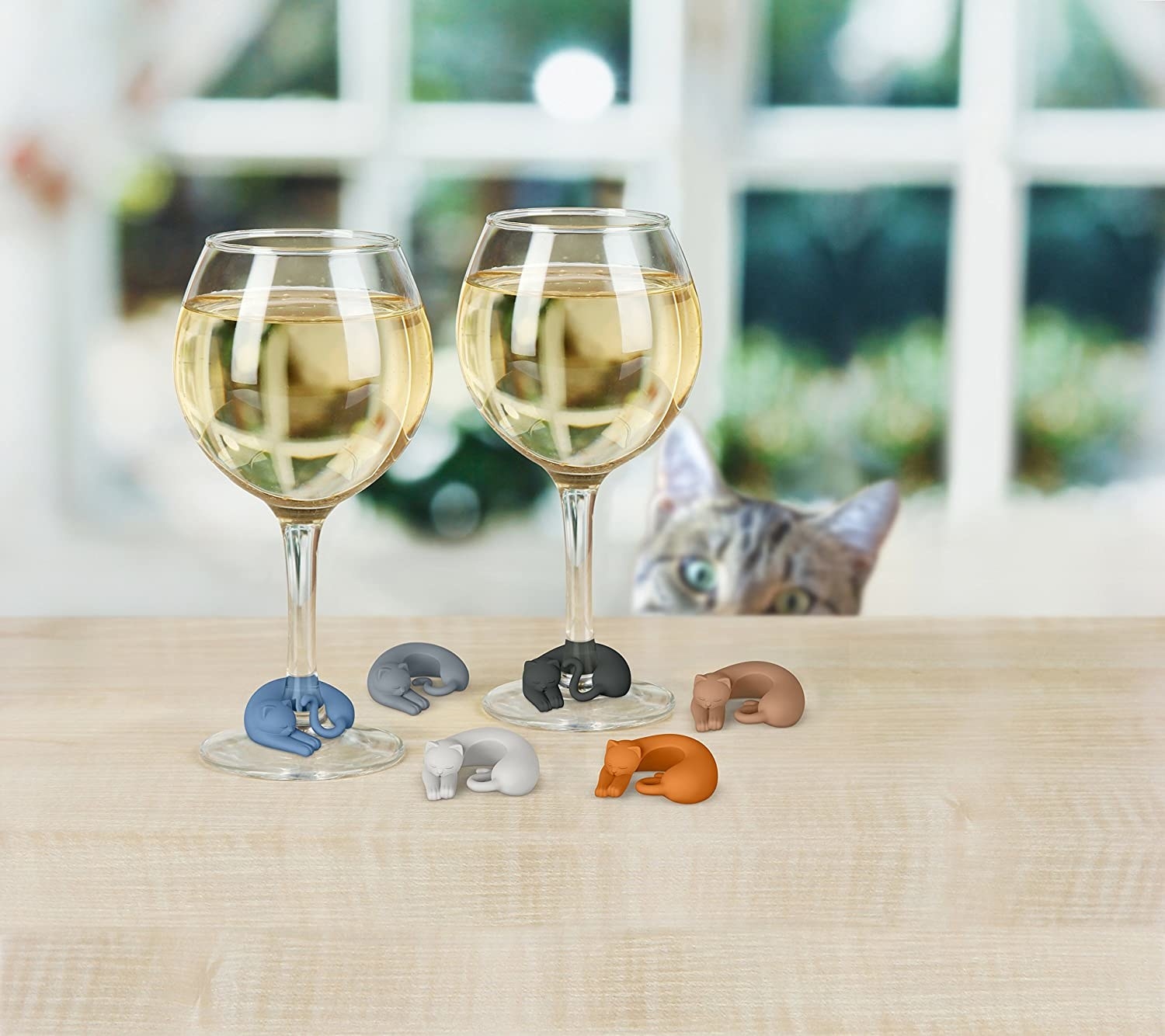 A set of cat-shaped wine markers curled around the stems of wine glasses