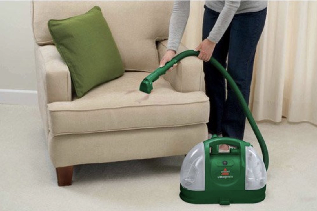 Model is using a green portable stain cleaner on a chair