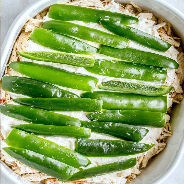Assembling the casserole with shredded chicken, cheese, and sliced jalapeños.