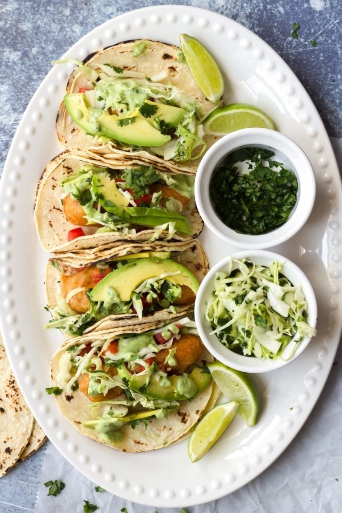 Three tacos filled with crispy fish and topped with avocado, slaw, and cilantro.